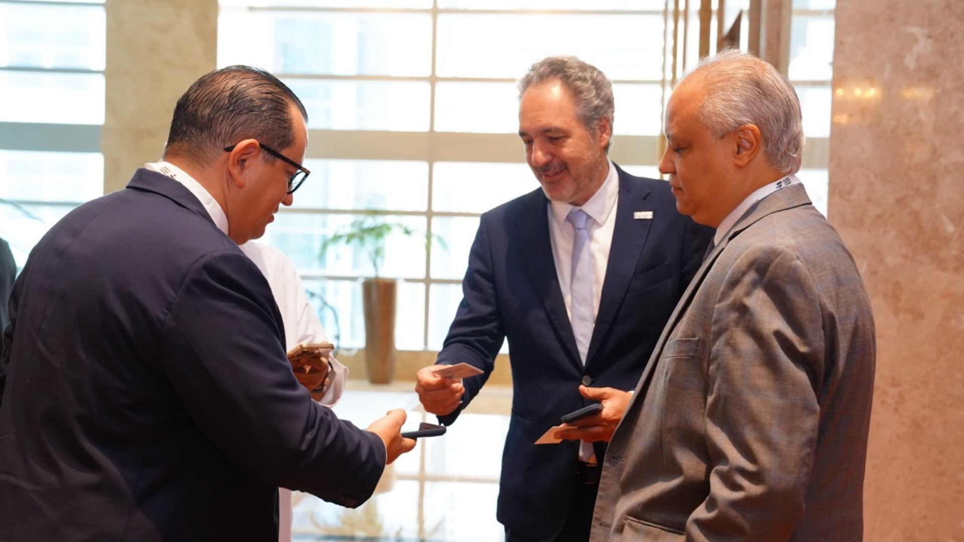 Three delegates exchanging contact details in a forum foyer